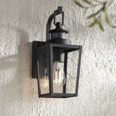 an outdoor light hanging on the side of a white stucco wall next to a plant