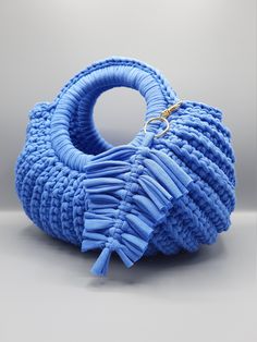 a blue handbag with tassels on the front and side, sitting on a gray surface