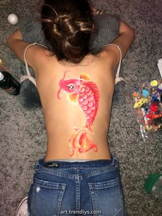 a woman with her back turned to the camera, has a fish painted on her stomach