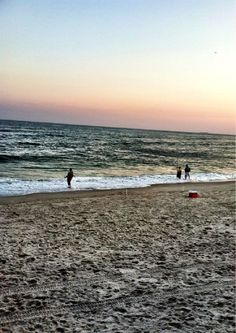 people are walking on the beach at sunset