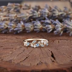 three stone ring sitting on top of a piece of wood with lavender flowers in the background