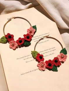 a pair of hoop earrings with red and pink flowers on them sitting on top of an open book