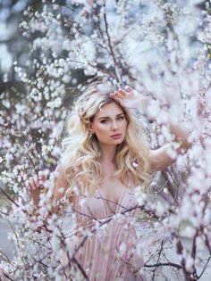 a woman standing in front of some trees with white flowers on her head and long blonde hair