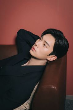 a young man sitting on top of a brown couch next to a red painted wall