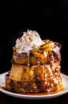 a stack of french toast with syrup and whipped cream on top, sitting on a plate