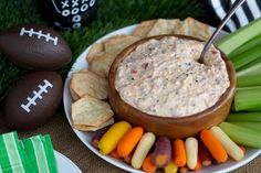 a bowl of dip surrounded by celery, carrots, and chips on a plate