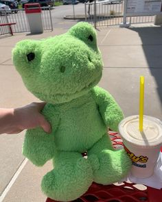 a green teddy bear sitting on top of a red cart next to a cup of coffee