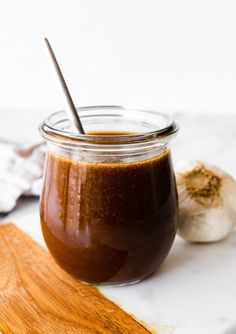 a jar filled with brown sauce sitting on top of a wooden cutting board next to garlic