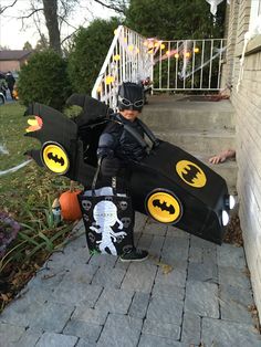 a young boy dressed up as batman with his homemade batmobile costume and pumpkins