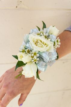 a woman's hand holding a bouquet of white and light blue flowers on her wrist