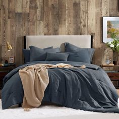 a bed with blue sheets and blankets on top of it in front of a wooden wall