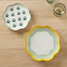 two green and yellow plates sitting on top of a wooden table next to glasses filled with water