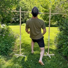 a man standing in front of a wooden frame on top of lush green grass covered ground