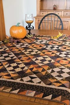 a table with a quilt on it and pumpkins sitting on the dining room table