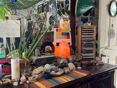 a table with many items on it in front of a wall full of pictures and plants