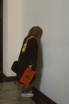 a person standing against a wall with their back to the camera and holding an orange book