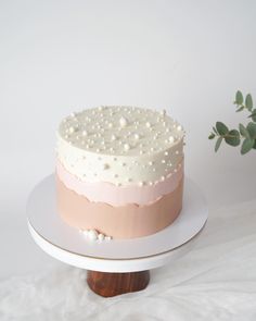 a white and pink cake sitting on top of a wooden stand next to a potted plant