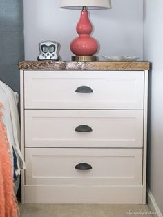 a white dresser with drawers and a lamp on top