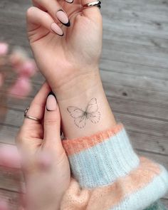 a woman's hand with a small butterfly tattoo on her left wrist and the other arm