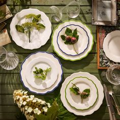 four plates with flowers and leaves on them sitting on a wooden table next to silverware