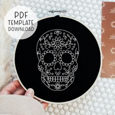 a hand holding a black and white cross - stitch pattern with a skull on it