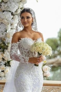 a woman in a wedding dress standing next to a flower covered archway with white flowers