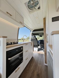 the interior of a camper with wood floors and white cabinets, including an oven