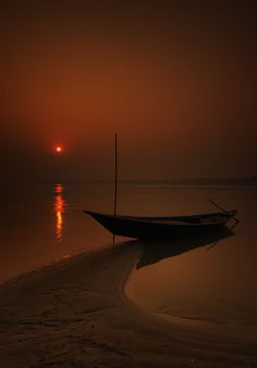 a boat sitting on top of a beach next to the ocean under a red sky