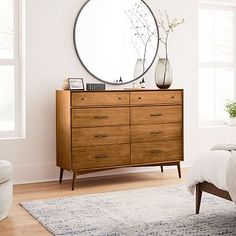 a bedroom scene with focus on the bed and dresser, which has a large round mirror above it