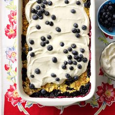 a blueberry cobbler with whipped cream in a white dish on a floral tablecloth