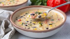 a spoon full of soup sitting in a bowl next to some tomatoes and other vegetables