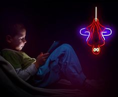 a young boy sitting in a chair looking at a tablet with a neon sign hanging above him