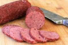 some sausages are on a cutting board with a knife next to it and another piece of meat in the background