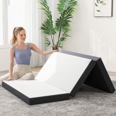 a woman sitting on the floor next to an upside down bed in front of a potted plant