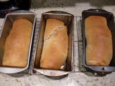 three loafs of bread sitting in pans on a counter top next to each other