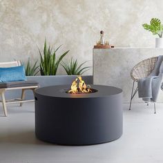 an outdoor fire pit sitting on top of a white floor next to a chair and potted plant