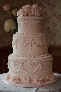 a three tiered wedding cake with pink roses on the top and pearls on the bottom