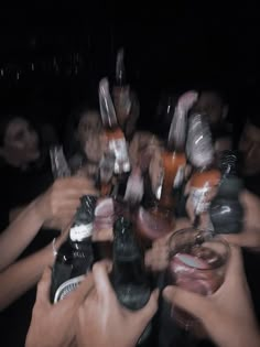 a group of people holding up bottles and glasses in the air with their hands together