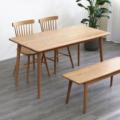 a wooden table and bench in a room with white walls, wood flooring and potted plant