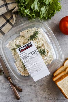 a plastic container filled with food next to bread and tomatoes