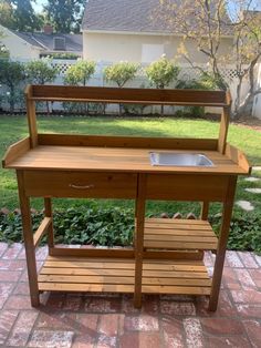 a wooden outdoor kitchen with sink and shelf on brick patio area in front of house