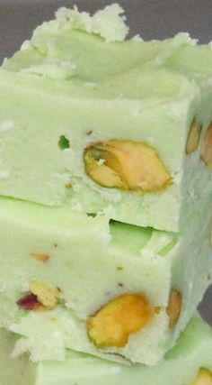 three pieces of green and white candy with nuts on top, stacked together in a pile