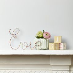 a white shelf topped with pink and green flowers next to a wooden block spelling the word ella