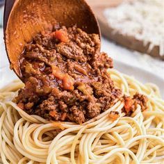 a wooden spoon full of spaghetti with meat sauce