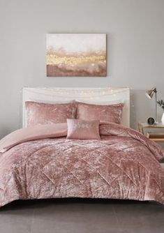 a bed with pink comforter and pillows in a room next to a painting on the wall