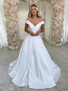 a woman wearing a white wedding dress standing in front of a flower covered archway with her hands on her hips