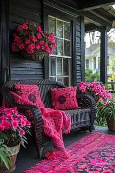 a porch with pink flowers and potted plants on the front steps, along with a black wicker couch