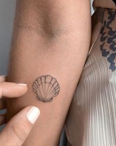 a woman's arm with a shell tattoo on the left side of her arm