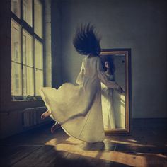 a woman is dancing in front of a mirror with her long hair blowing in the wind