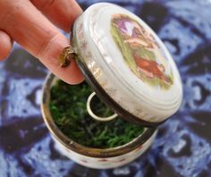 "The lid of this antique round porcelain pill box is hand painted with a classical scene, and the sides have tiny red roses with blue swags. It is signed Angelica Kauffman.  It has a gold tone metal edges and a tidy hinge.  It shuts securely and opens easily.  I'm pretty sure it was made in France during the latter half of the 19th century.  Measures 3\" diameter and 1 3/4\" high.  Excellent condition with no chips, cracks or repairs. I have lined it with moss to provide a soft bed of moss so al Unique Ring Box, Antique Ring Box, Vintage Ring Box, Ring Bear, Romantic Rings, Soft Bed, Ring Boxes, Engagement Ring Box, Porcelain Jewelry